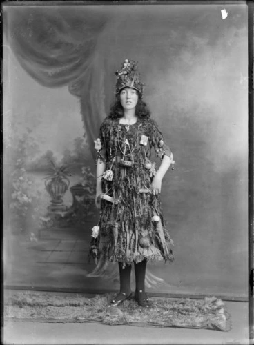 Image: Studio portrait of unidentified young woman in Christmas tree fancy dress and hat costume, with little presents and decorations hanging off her, Christchurch