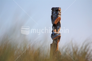 Image: Carving of Matariki in background behind beach grass in soft focus.