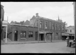 View of large brick building with R Taylor & Co Boot Repairer and Thomas Bain Newsagents, Dannevirke, Hawke's Bay District
