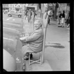 Unidentified woman sitting in a folding chair next to a parking metre, [waiting for?] Festival of Wellington parade