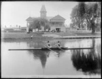 Unidentified men's double coxed rowing team from Avon Rowing Club on Avon River, Christchurch, includes boat shed and other rowing club members in background