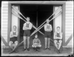 Unidentified men's coxed four rowing team with a young boy coxswain, with crossed oars behind, outside the Avon Rowing Club boatshed, Christchurch