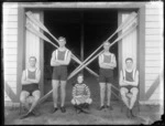 Men's coxed four unidentified rowing team with a young boy coxswain, crossed oars behind, outside the Avon Rowing Club boatshed, Christchurch