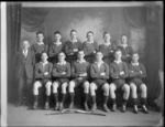 Studio portrait of a men's hockey team, unidentified players in uniforms and coach with hockey sticks in front, Christchurch
