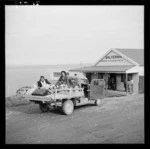 Two women sitting on the back of a utility vehicle outside Walker Bros general store, Te Kaha