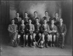 Studio portrait of unidentified men's hockey team and coaches, probably Christchurch district, includes two cup trophies and hockey sticks in the front