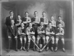 Studio portrait of unidentified youth hockey team in uniforms and coaches, with pads, hockey sticks and mediun size cup in front, Christchurch