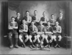 Studio portrait of unidentified young men's hockey team in uniforms and coaches, with pads, hockey sticks and two cup in front, Christchurch