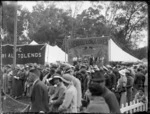 Day at the races with crowd looking on, stage behind with mid-race entertainment troop 'The Aerial Lorraines flying trapeze artists', Puketapu, Hastings, Hawke's Bay District