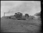 View of The Hawke's Bay Farmer's Freezing Works, Whakatu, showing the freezing works buildings with road and field in front, Hastings, Hawke's Bay District