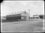 External view of the British Imperial Oil Co Ltd brick building with advertising signs for Shell Spirit and Shell Kerosene, with railway street crossing in front and other commercial buildings beyond, probably Christchurch region