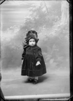 Studio Slater family portrait of a toddler girl standing in a dark patterned dress with large collar and bow with matching pleated hat with ribbon, Christchurch