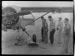 Sir Edmund Hillary in pullover (centre) and Harry Wigley (left) inspecting undercarriage of Antarctic Beaver Ski Plane with four unidentified men, Mount Cook Airfield, Mount Cook National Park, Canterbury Region