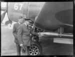 Royal New Zealand Air Force AVM LM Isitt and Wing Commander R Webb inspecting rockets on an aeroplane, Ardmore Airport, Auckland