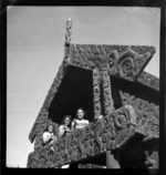 Unidentified Maori girls sitting in carved Pataka wearing traditional dress and with poi, Whakarewarewa, Rotorua