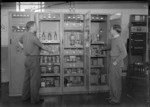 Interior view of the Transmission House, Musick Point Air Radio Station, Howick, Auckland, showing two unidentified men checking transmission cabinets