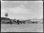 New Zealand National Airways Corporation Lockheed Electra 'Kahu', ZK-AGJ, twin engine passenger plane, at Rongotai Airport, Wellington, also showing traffic control tower, another plane and refueling trailer