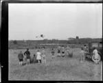 View of unidentified children watching Auster J-1B Autocrat ZK-AOB passenger plane taking-off from [river flats?], Balclutha, Otago Region