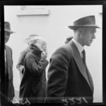 Accused murderess, with scarf obscuring face, surrounded by unidentified men, at Wellington Magistrates Court