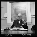 Portrait of Percy Coyle, smoking a cigarette at his desk, Wellington