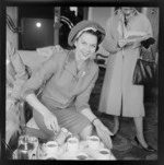 Portrait of ballet dancer Pamela Moncur from England pouring a cup of tea within an unknown building location, probably Wellington City