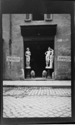 Statues, including a female, male and two lions in a shop door, with the number '160' and 'La Cerimonia Al Colosseo E Rimandata A Giorno Da Destinarsi' written on the concrete wall, Rome, Italy