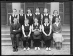 Girls' netball team with small cup trophy, and two teachers from Westport Technical High School (WTHS), outside brick building, West Coast Region