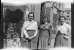 Three unidentified young female employees of Andrew Lees Ltd, supplier of paperhangings, paint and glass, standing outside business premises, cans of paint on display in shop window behind