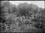 Stewart Island. Albert Percy Godber and a woman (possibly his daughter Phyllis) standing in the bush.