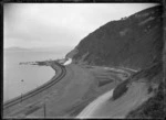 View of a train rounding Rocky Point in 1908 after the track was moved nearer the harbour following partial reclamation, between Wellington and Petone.