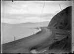 View of a train rounding Rocky Point after the track was moved nearer the harbour following partial reclamation, between Wellington and Petone.