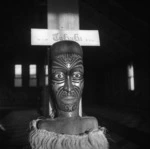 Head of a Maori wooden carved figure on the ridge pole of a meeting house in Te Kaha