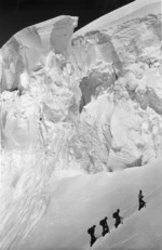 Four mountaineers climbing a snow covered slope beneath ice cliffs