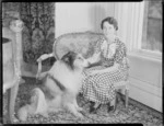 Jean Sutherland seated with collie inside at Homewood, Karori, Wellington
