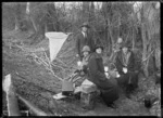 Group having a picnic in bush beside the Taieri River, with a whitebait net nearby.