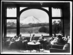 People in a lounge at Chateau Tongariro with Mount Ngauruhoe visible through the window - Photograph taken by Leslie Hinge
