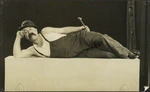 Man lying on his side holding a hammer - Photograph taken by R E Collett
