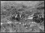 Group of men with their dogs, around a camp fire. The man second from left holds a wild piglet in his lap. On the Mendip Hills sheep farm.