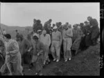 South African golfer Bobby Locke and New Zealand golfer Bob Charles surrounded by a crowd dressed for bad weather at Miramar Golf Course, Wellington