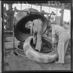 Unidentified workers fitting tyre on to press, Dunlop rubber factory, Upper Hutt