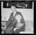 Mr Toop and his mother [Mrs Toop] sitting on a chair in a sitting room