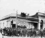 Crowd outside the tobbaconist shop of R Farmer, on the corner of Perry and Queen Streets, Masterton