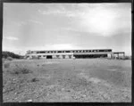 Poultrymen's Co-Operative Penrose site showing a large vacant site with a Fletcher merchants shed filled with timber, with the sign 'wood is wonderful' above, Auckland