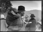 Maori woman eating watermelon and carrying a young child wrapped in a blanket on her back