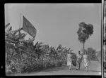 Mrs H Goodsell, T Greenup, and [Mr A Licherand?] walking in Berrimah garden, including Qantas Empire Airways flag, Darwin, Australia