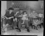 Sir Peter Buck sitting next to two women in the meeting house and holding a little girl, Ngaruawahia, Waikato