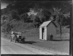 Walter Strawbridge beside a corrugated shed labeled 'Oaro Post Office', Kaikoura coast; another man is in a Singer car on the road beside.