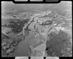 View down Clutha River from Roxburgh Dam site, Central Otago, showing excavation of diversion channel with heavy earth moving machinery, workers accommodation and site buildings and road down valley beyond