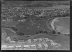 Orakei, Auckland, view of Maori settlement at Orakei Domain, Okahu Bay, with beach and Tamaki Drive with several houses and meeting house on scrubland foreground, residential houses surround with Hobson Bay beyond