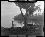 Unidentified man in boat at Faleolo, Apia, Upolu, Samoa, showing fales and palm trees